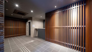 Un hall d’hôtel moderne avec un comptoir d’accueil, une cloison en lattes de bois et un sol carrelé.