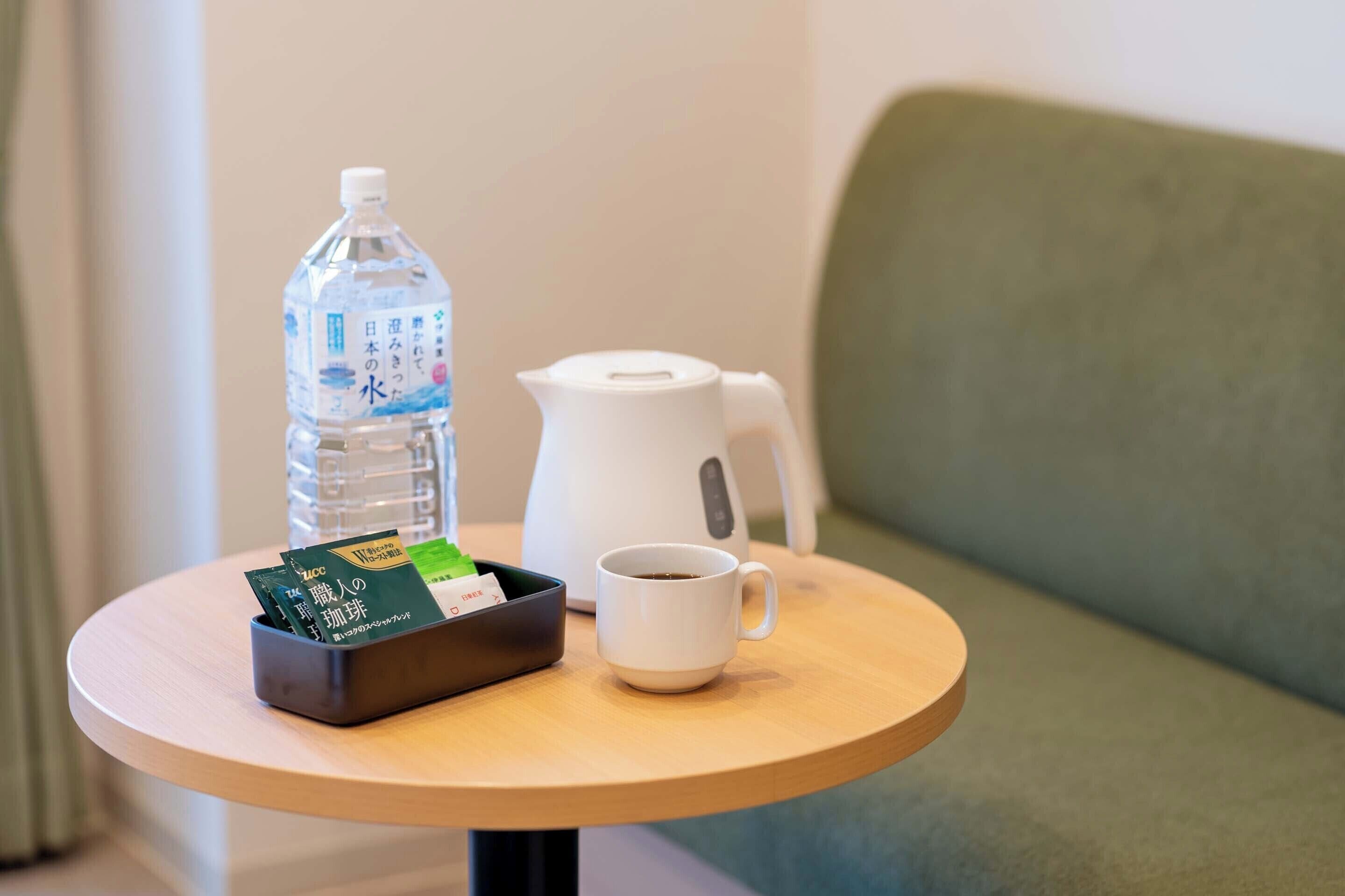 A small round table with a water bottle, a white coffee pot, and a cup of coffee.
