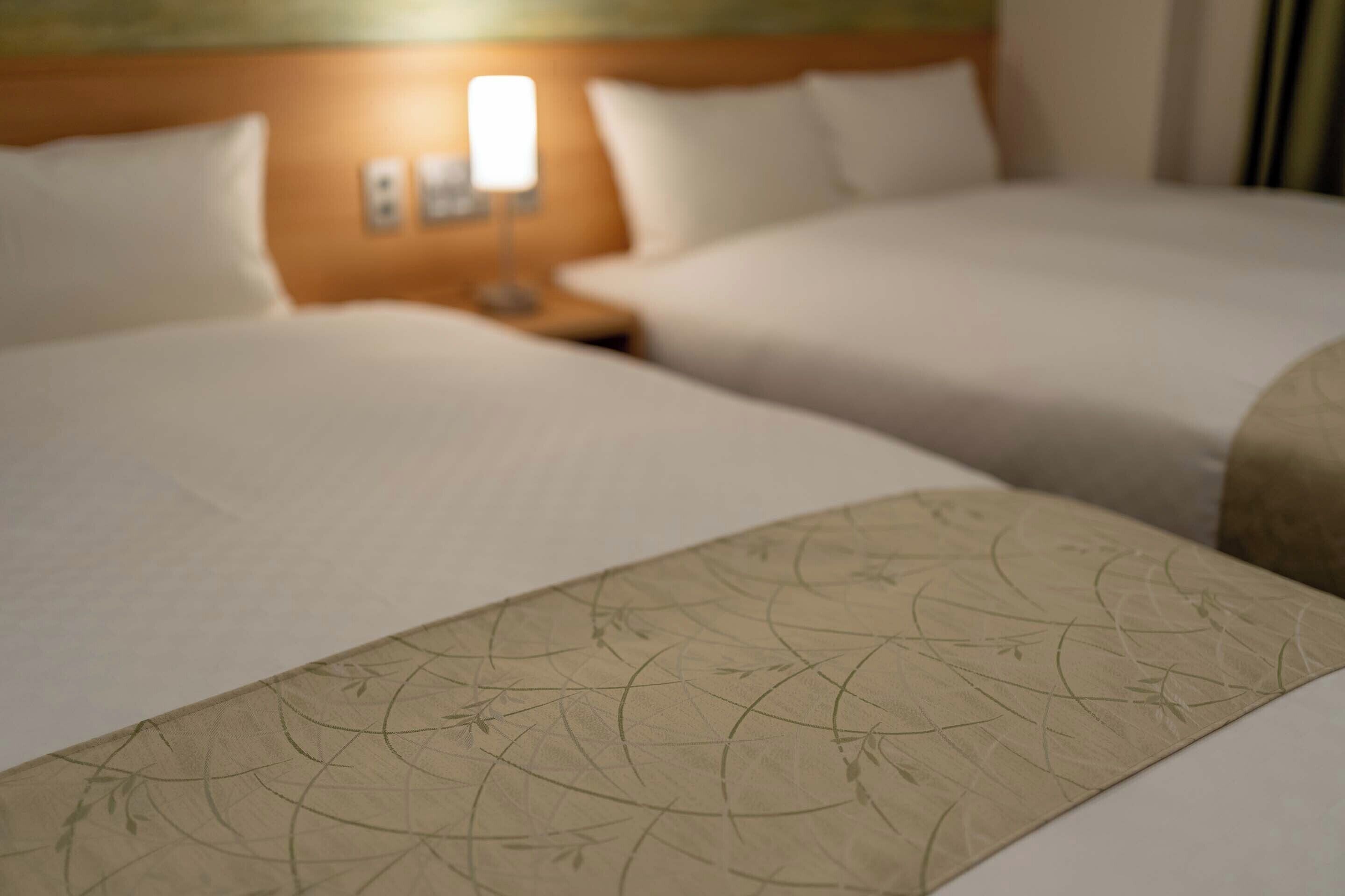 Two hotel beds with white linens and a nightstand with a lamp.