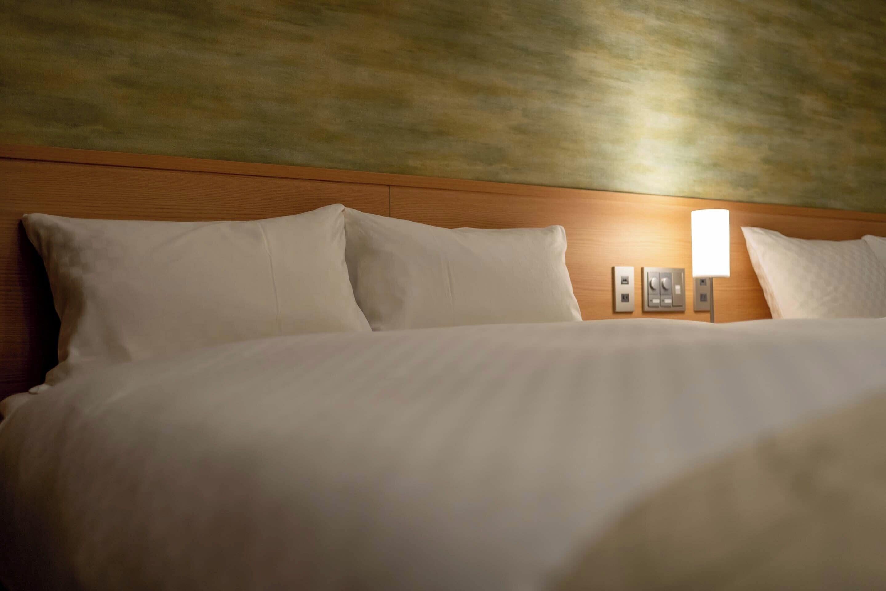 A hotel room with a wooden headboard, white bedding, and a wall-mounted light fixture.