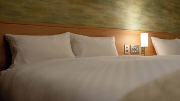 A hotel room with a wooden headboard, white bedding, and a wall-mounted light fixture.