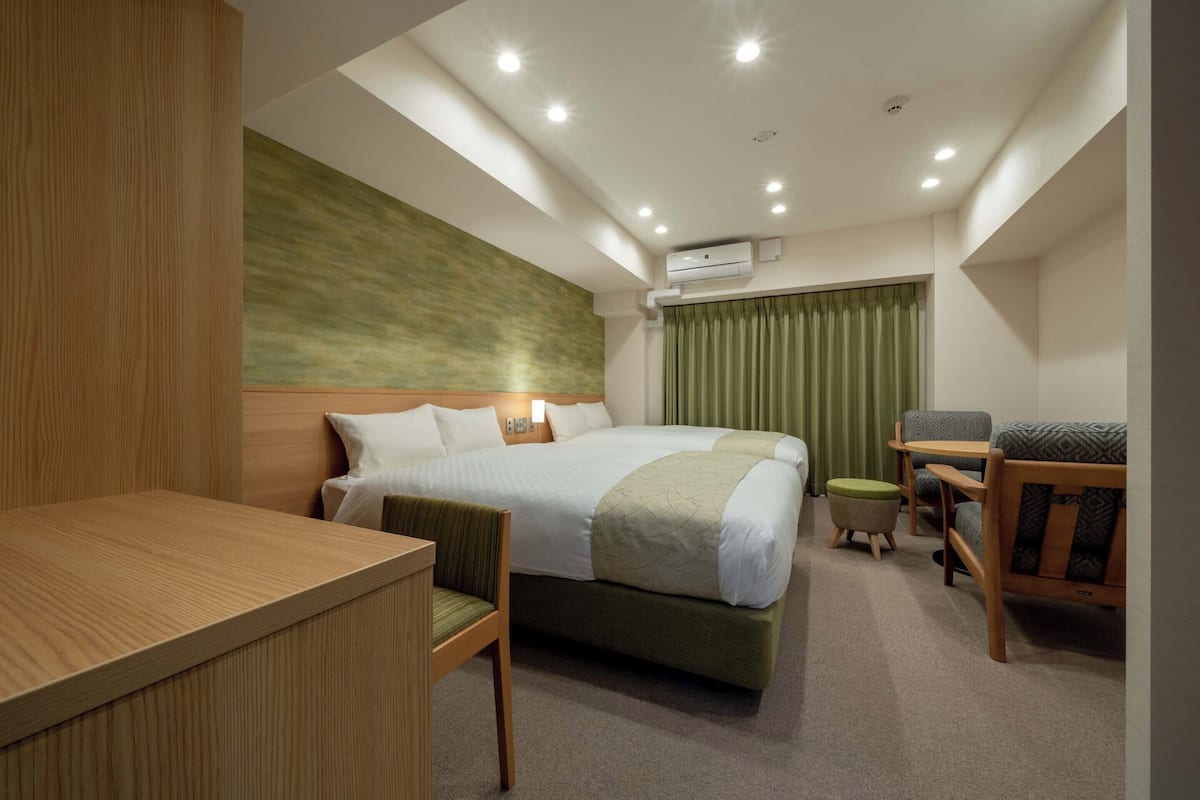 Ein Hotelzimmer mit Bett, Schreibtisch, Stuhl, einem kleinen Tisch und einem grünen Vorhang.