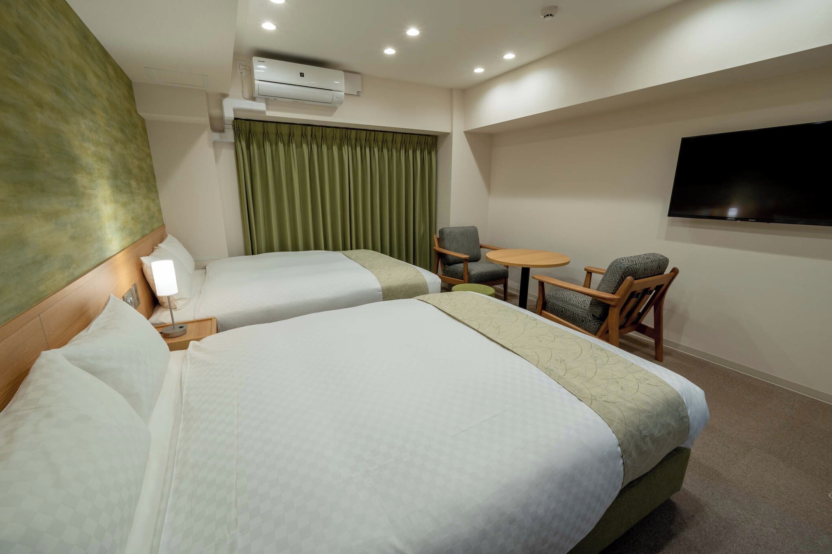A hotel room with two beds, a television, a small table, and a chair.