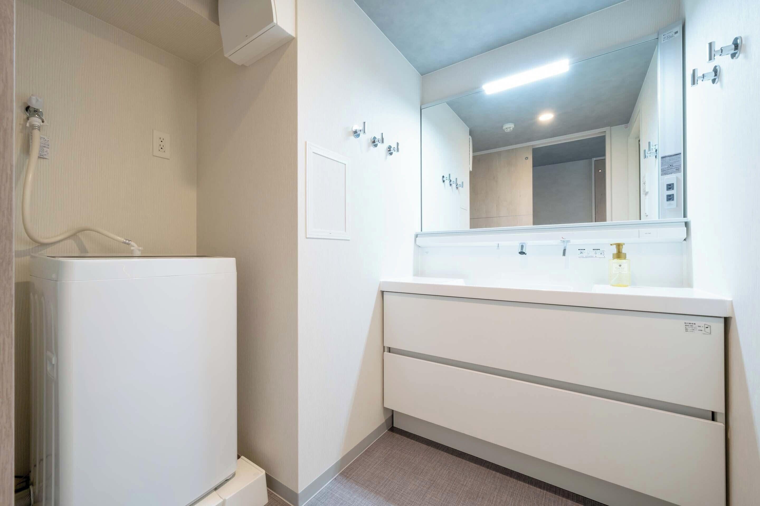 Un baño con lavamanos, espejo y calentador blancos.