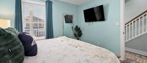 Un dormitorio con cama, televisión, ventana con cortinas y una escalera.