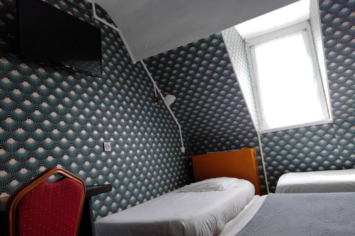Una habitación pequeña con una cama litera, una cama individual, una silla roja y una ventana.