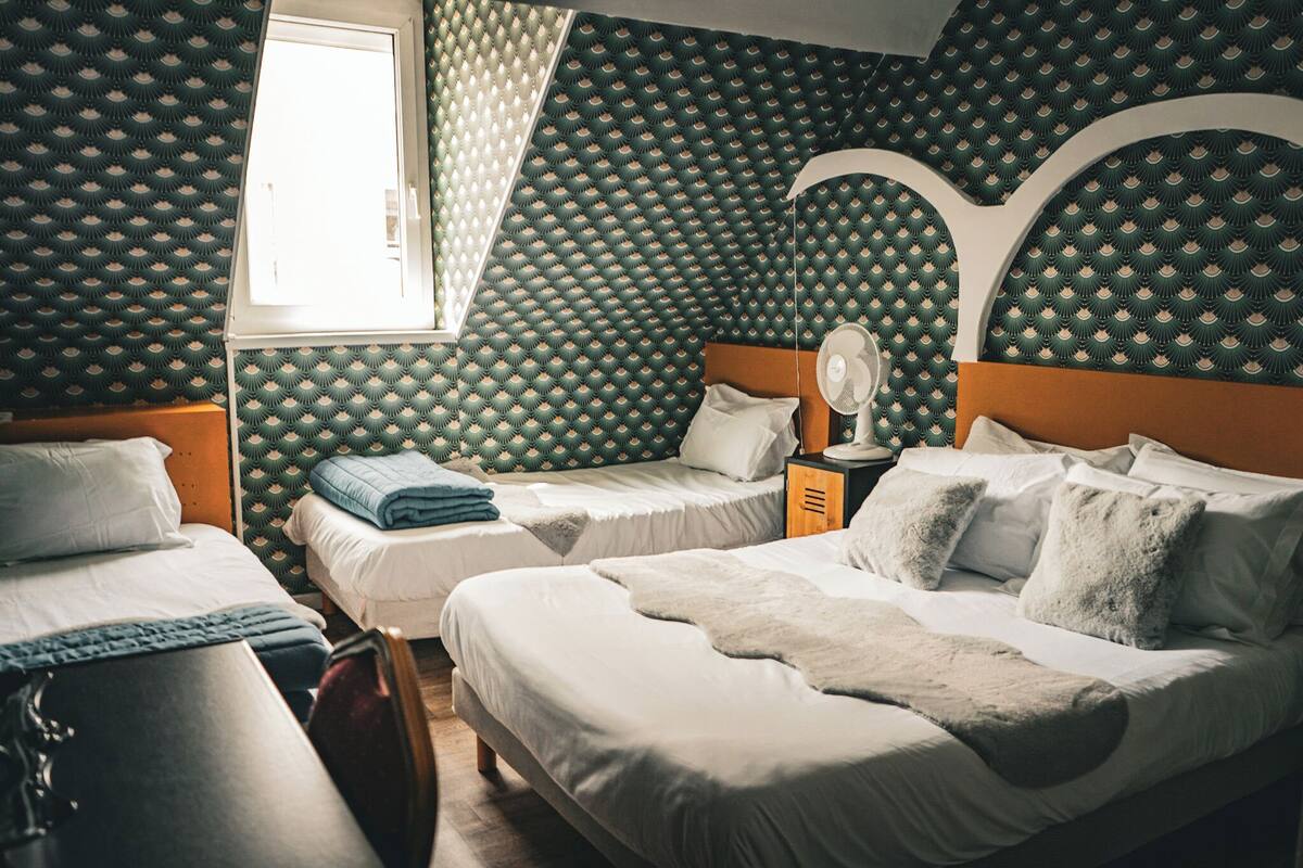 Una habitación con tres camas, una ventana y papel tapiz estampado.