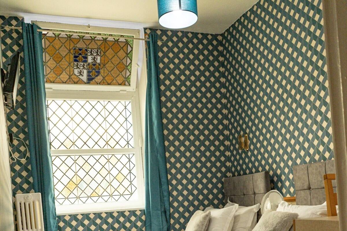 Un dormitorio con cama, ventana con cortinas, radiador y pared con diseño.