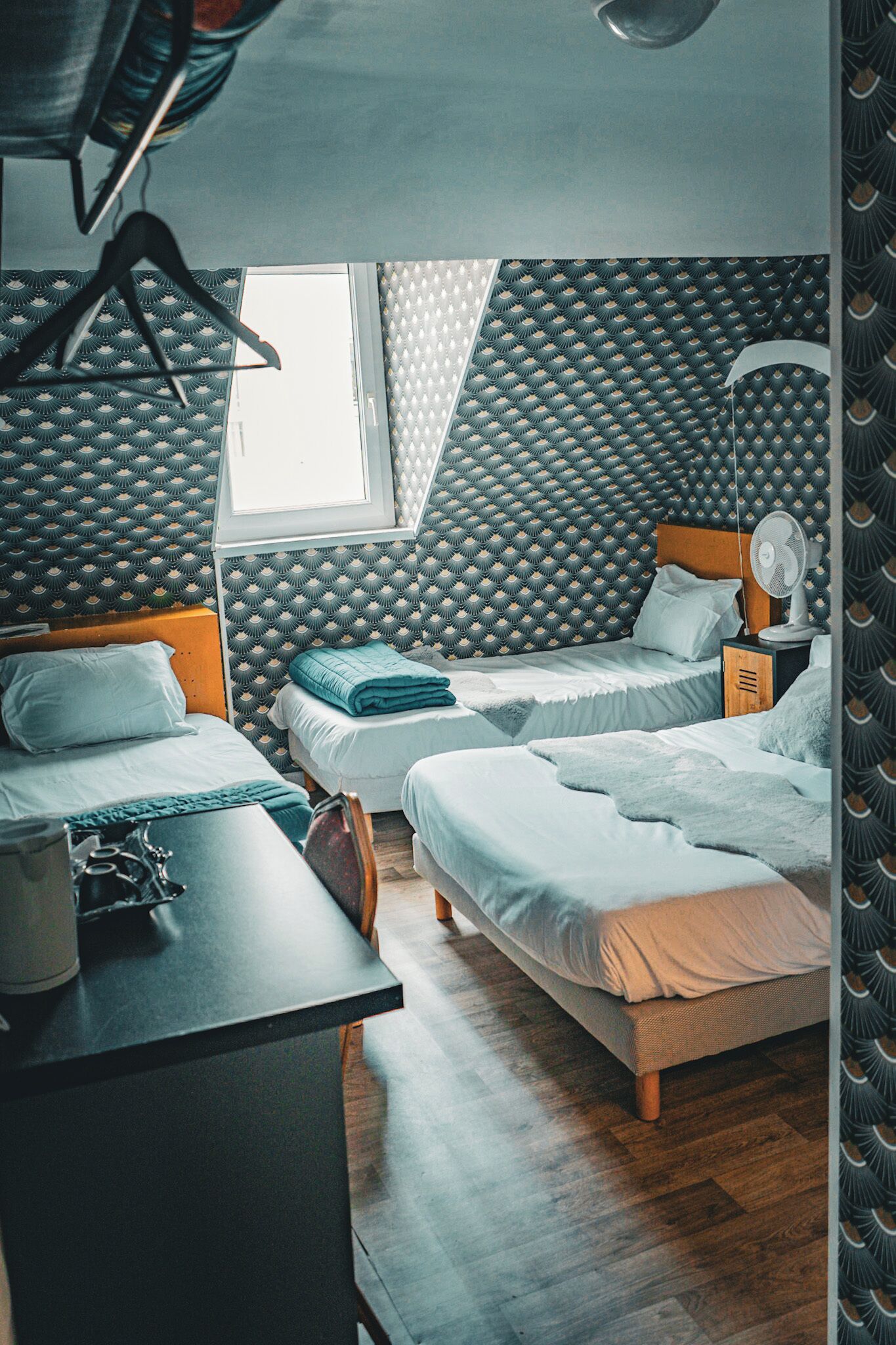 Een kamer met twee bedden, een bureau, een stoel, een kapstok en een raam.