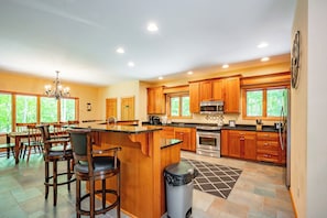 A modern kitchen with wooden cabinets, a central island, and a dining area with chairs.