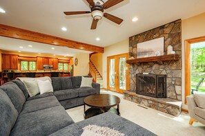 Una sala de estar con chimenea de piedra, ventilador de techo y un amplio sofá seccional gris.