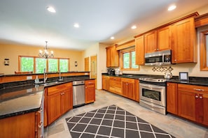 A modern kitchen with wooden cabinets, stainless steel appliances, and a chandelier.