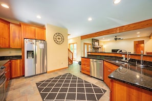 A kitchen with wooden cabinets, a stainless steel refrigerator, a clock, and a tiled floor.