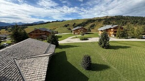 Vista de un albergue de montaña con varias cabañas de madera, un césped cuidado y colinas y montañas al fondo.