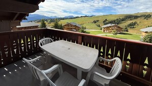 Un balcón con mesa y sillas, con vistas a un paisaje rural con casas y montañas.