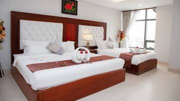 A hotel room with two beds, a large wooden headboard, a window with curtains, and a framed picture on the wall.