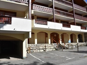 Un edificio de varios pisos con balcones, una escalera de piedra y un área de estacionamiento.