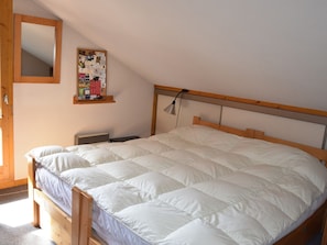Ein Schlafzimmer mit einem hölzernen Bett, einem Nachttisch, einer Wandtafel und einem Spiegel.