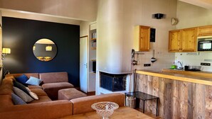 A living room with a sofa, a round mirror, a wooden table with a glass bowl, and a kitchen area with wooden cabinets and a microwave. - Sunny 4-room apartment, south balcony, near cable car (Pralognan-la-Vanoise)