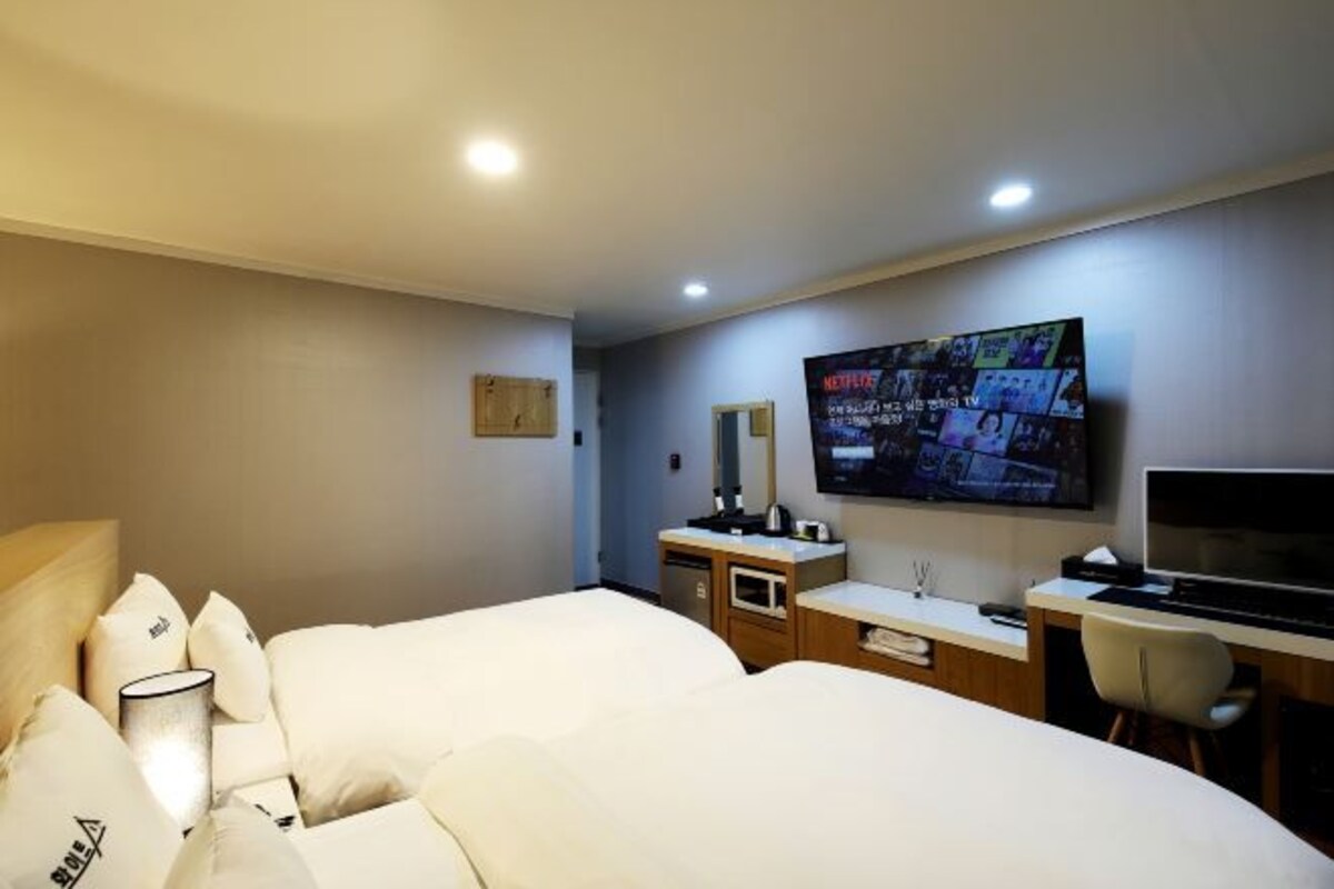 A hotel room with two beds, a desk, a TV, and a minibar.