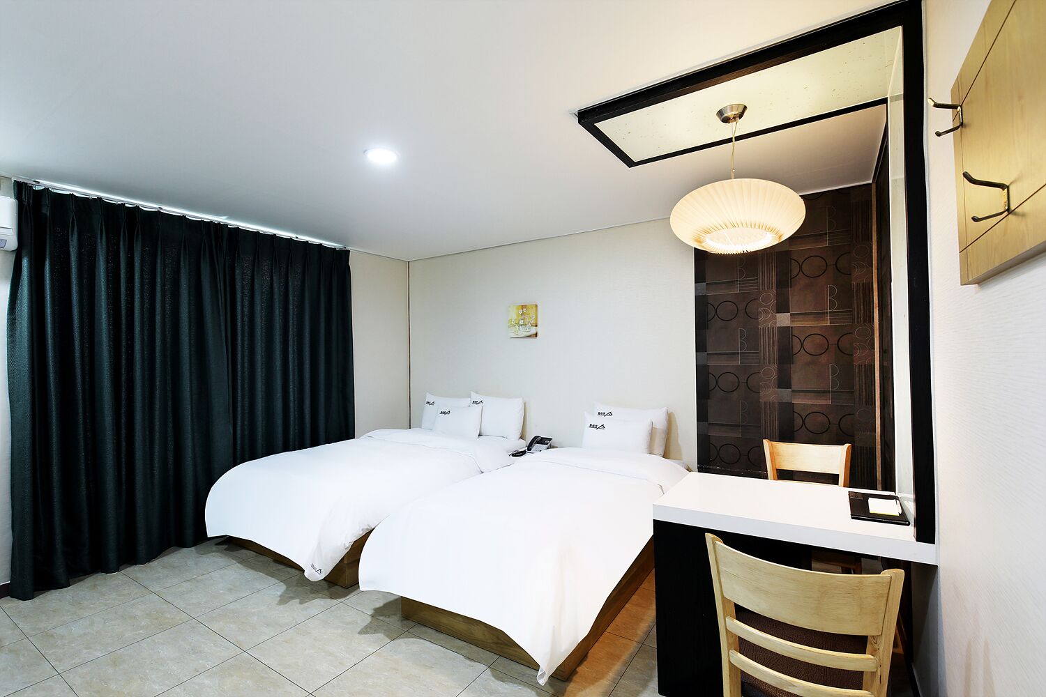 A hotel room with a bed, bedside table, chair, and a large mirror.