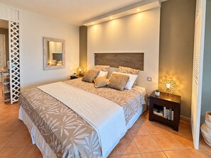 A bedroom with a large bed, a nightstand with a lamp, a bookshelf, and a mirror on the wall. - Caribbean Escape - View Orient Bay and St Barth, pool and beach - 4217 (Orient Bay)