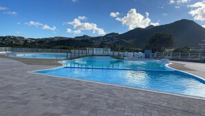 A swimming pool with a bridge, surrounded by a paved area and a mountainous landscape in the background. - Caribbean Escape - View Orient Bay and St Barth, pool and beach - 4217 (Orient Bay)