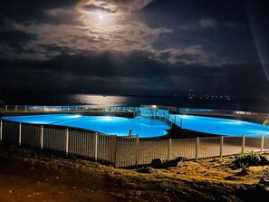 A large, illuminated swimming pool at night with a view of the ocean and a bridge in the background. - Caribbean Escape - View Orient Bay and St Barth, pool and beach - 4217 (Orient Bay)