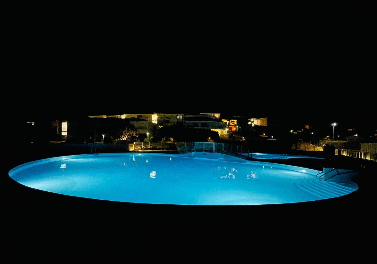 A nighttime view of a swimming pool with a clear view of the surrounding buildings and landscape.
