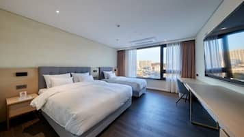 Habitación de hotel con dos camas, un escritorio y un amplio ventanal con vistas a la ciudad.