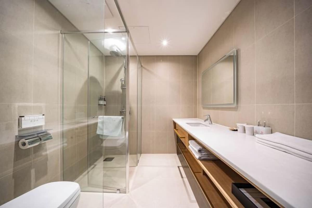 Un baño moderno con ducha de vidrio, lavamanos blanco y un espejo grande.