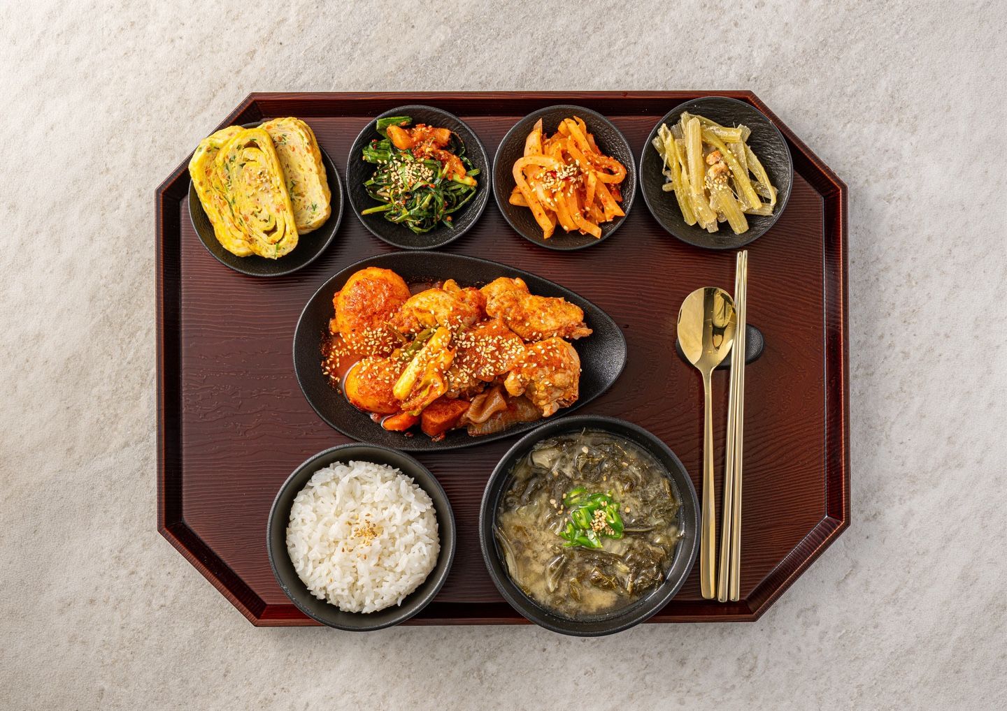 Una bandeja con diversos platos coreanos, como arroz, sopa y verduras salteadas.