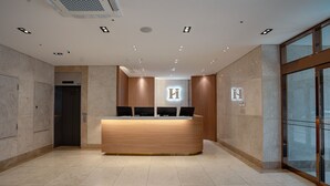 A modern reception desk with a wooden finish, a glass door entrance, and a visible elevator. - Gwangju H1 Hotel (Gwangju)