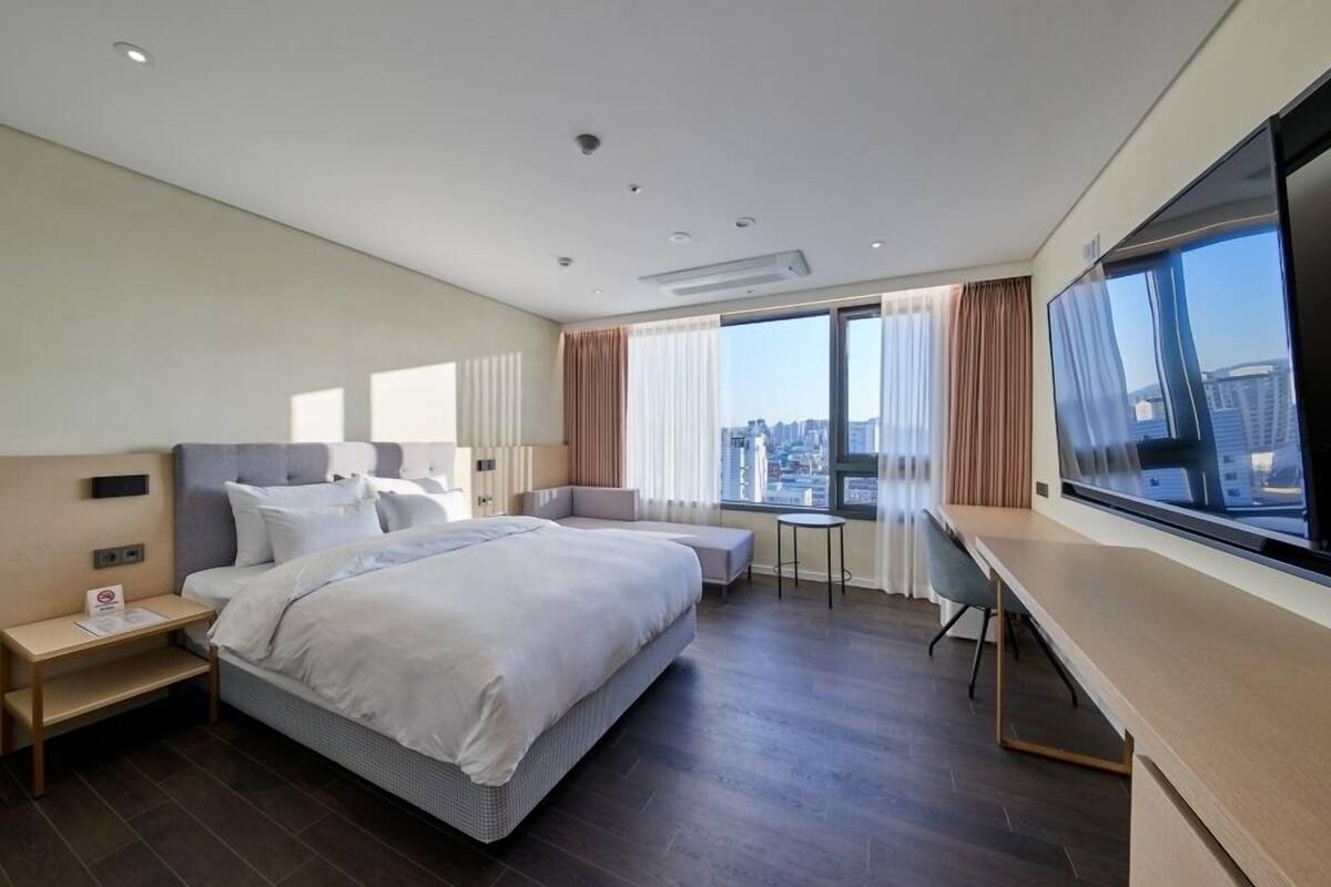 A modern hotel room with a large bed, a desk, and a TV.