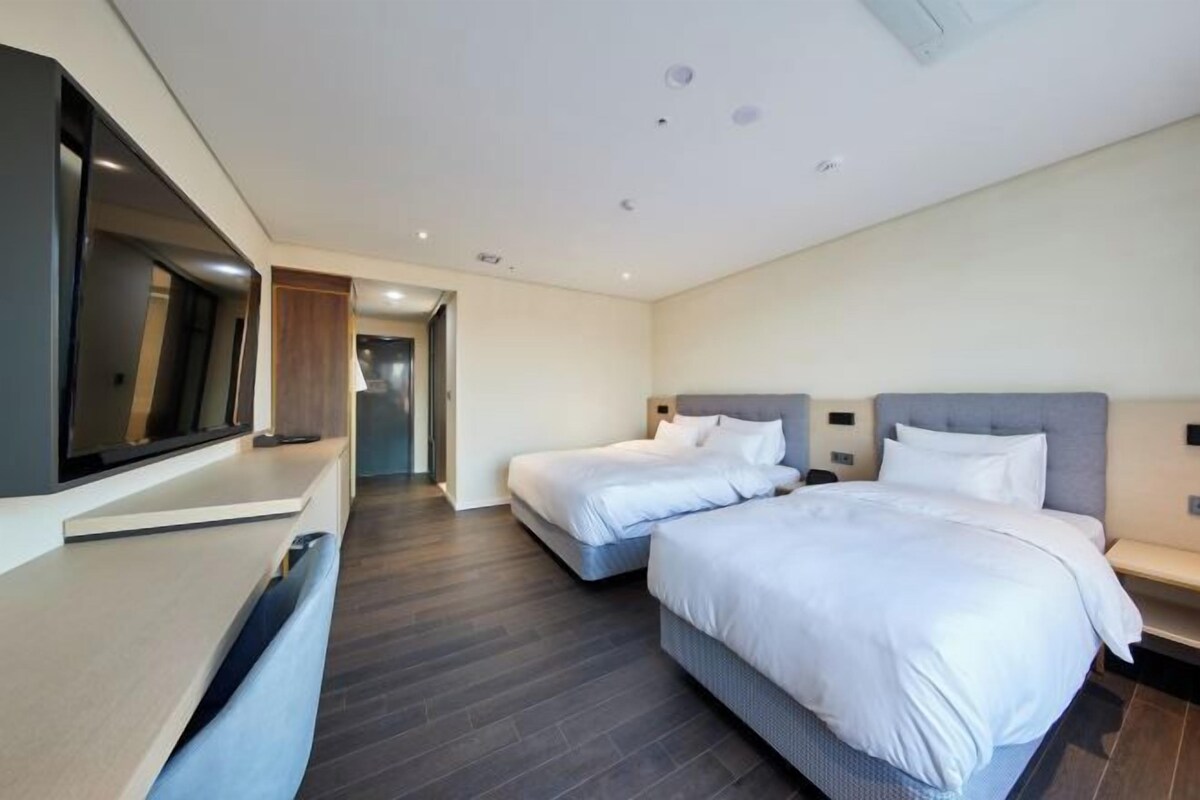 Une chambre d’hôtel moderne équipée de deux lits, d’un téléviseur à écran plat et d’un bureau.