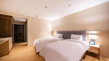 A hotel room with two beds, wooden flooring, a wardrobe, and a bedside table with a lamp.