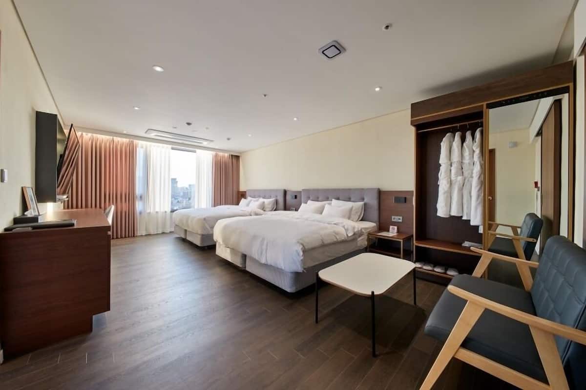 A hotel room with two beds, a desk, a chair, a wardrobe, and a large mirror.