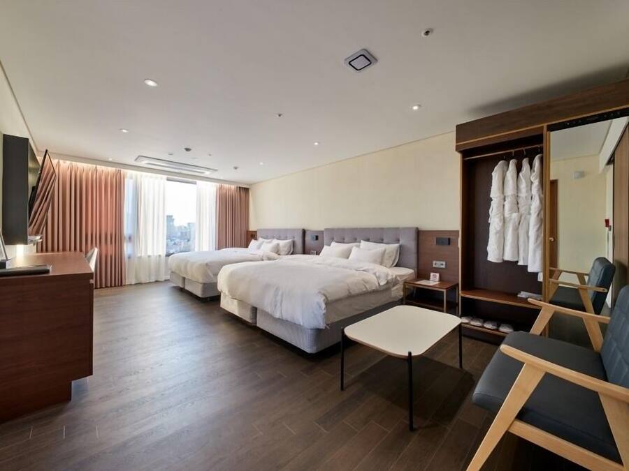 A hotel room with two beds, a desk, a chair, a wardrobe, and a large mirror.