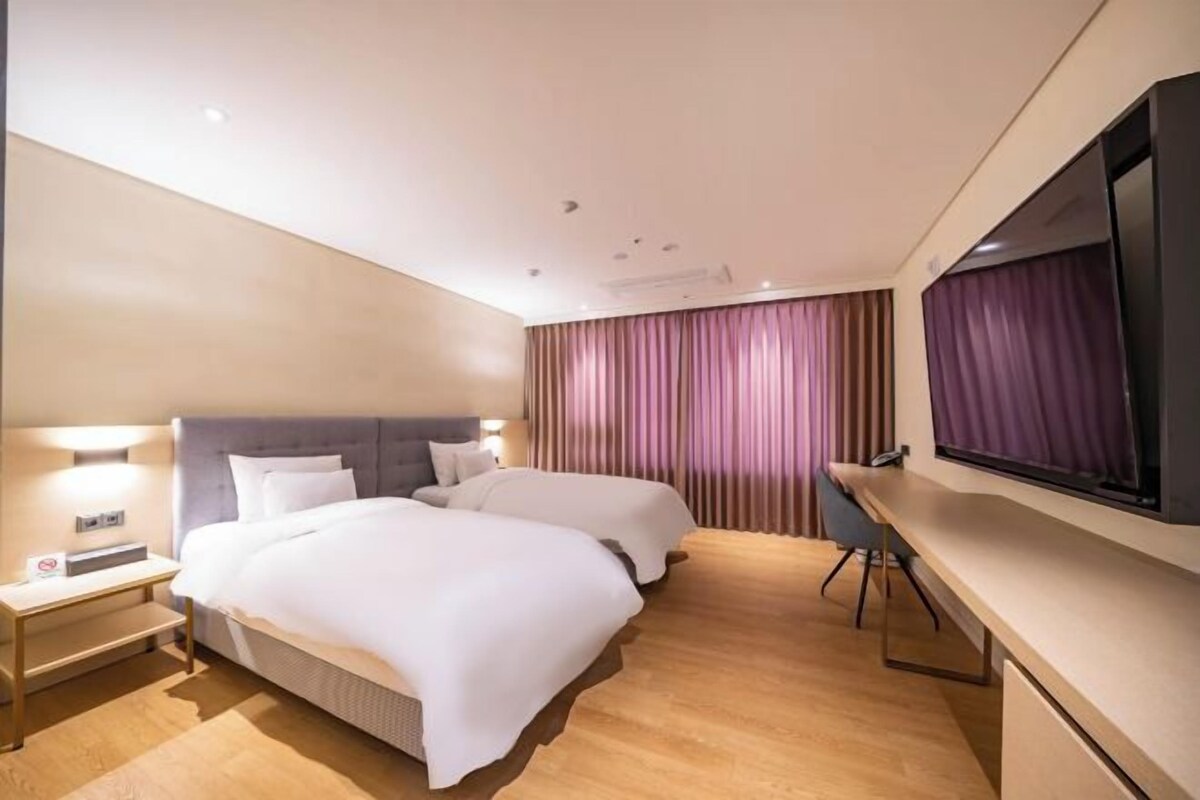 A hotel room with two beds, a desk, a TV, and a curtain.