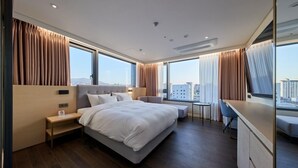 A modern hotel room with a large bed, a desk, and a view of the city. - Gwangju H1 Hotel (Gwangju)