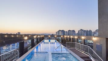 A rooftop pool with a view of the city skyline at dusk.