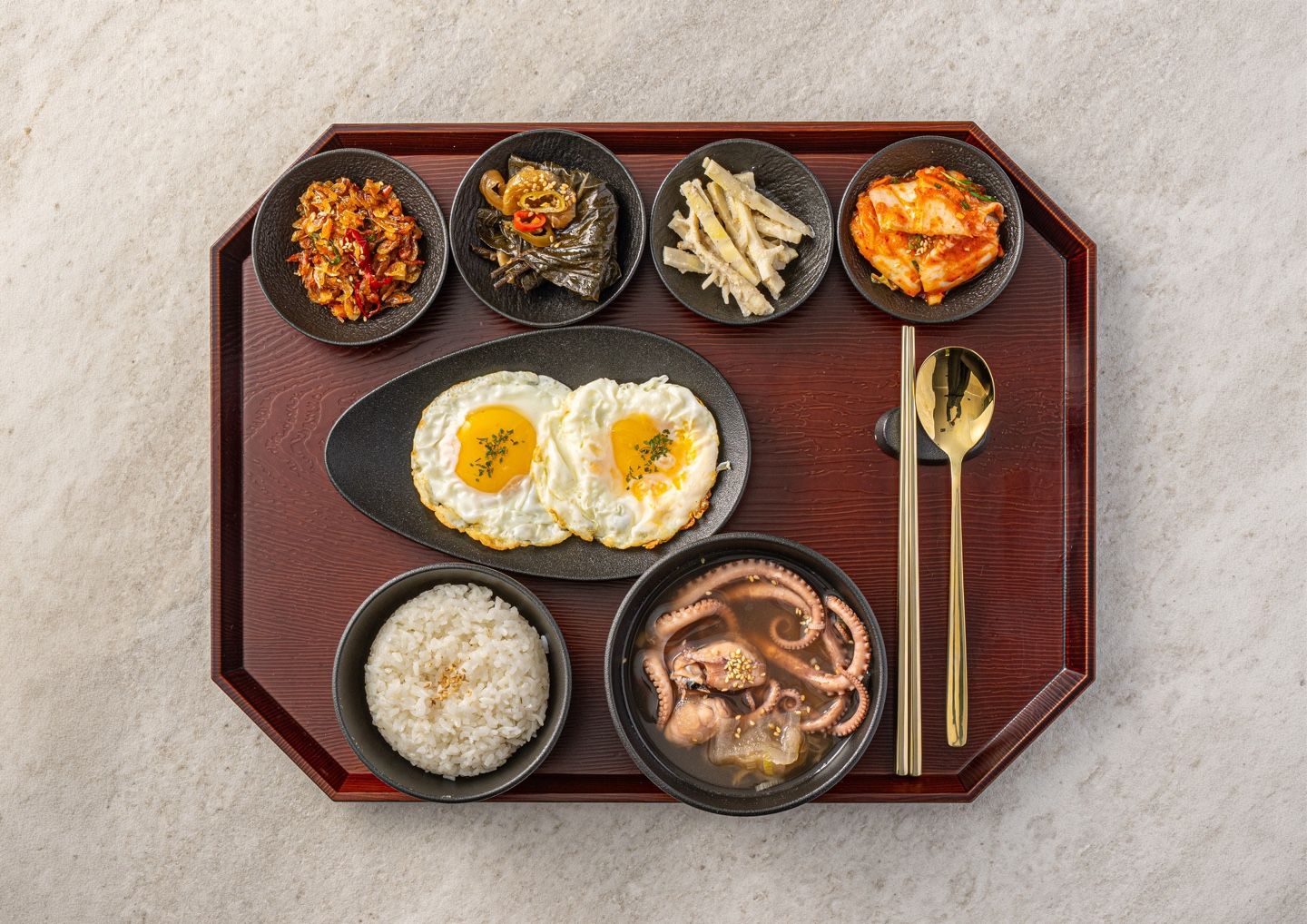 A tray with various dishes including fried eggs, rice, octopus, and other items.