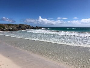 A beach with clear blue water, a sandy shore, and rocky outcrops.