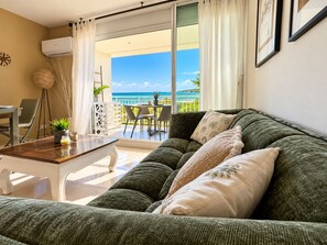 A cozy living room with a green sofa, a coffee table, and a view of the ocean through a sliding glass door. - Rêves de Tropiques - Studio 4309: Breathtaking Ocean View (Orient Bay)
