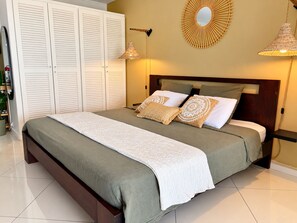 A bedroom with a bed, a wardrobe, and a wall-mounted circular mirror. - Rêves de Tropiques - Studio 4309: Breathtaking Ocean View (Orient Bay)