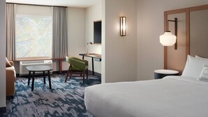 Habitación de hotel con una cama grande, un escritorio con silla, una mesita pequeña y un ventanal con cortinas.
