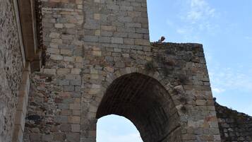 Una torre de piedra con un reloj, un arco y montañas al fondo.