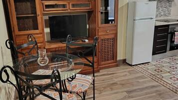 Een keuken met een eettafel, stoelen, een televisie, houten kastjes en een inbouwfornuis.