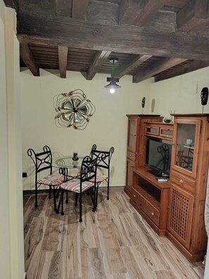 Un coin repas comprenant une table ronde, quatre chaises, un ventilateur de plafond et un meuble en bois abritant un téléviseur.