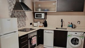 A compact kitchen with a microwave, toaster, sink, and a washing machine. - Apartamentos EL Wala (Hervás)